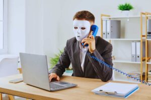 un uomo con una maschera bianca che fa una telefonata ed è al computer