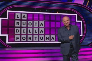 gerry scotti di fronte al tabellone della ruota della fortuna