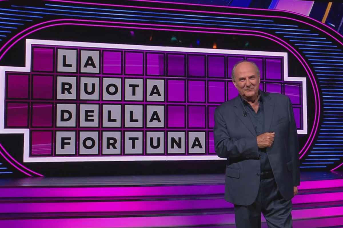 gerry scotti di fronte al tabellone della ruota della fortuna