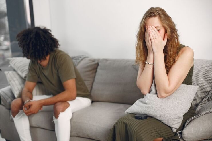 Donna con mani sul viso seduta sul divano, uomo seduto accanto ma guarda altrove